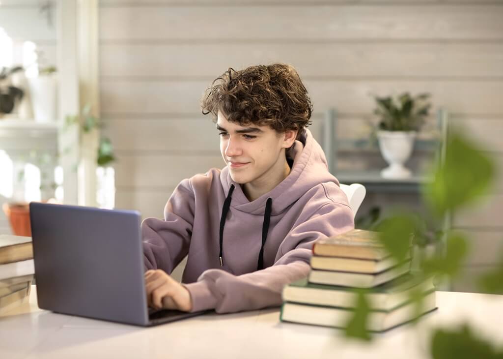 rapaz mexendo em computador ao lado de livros